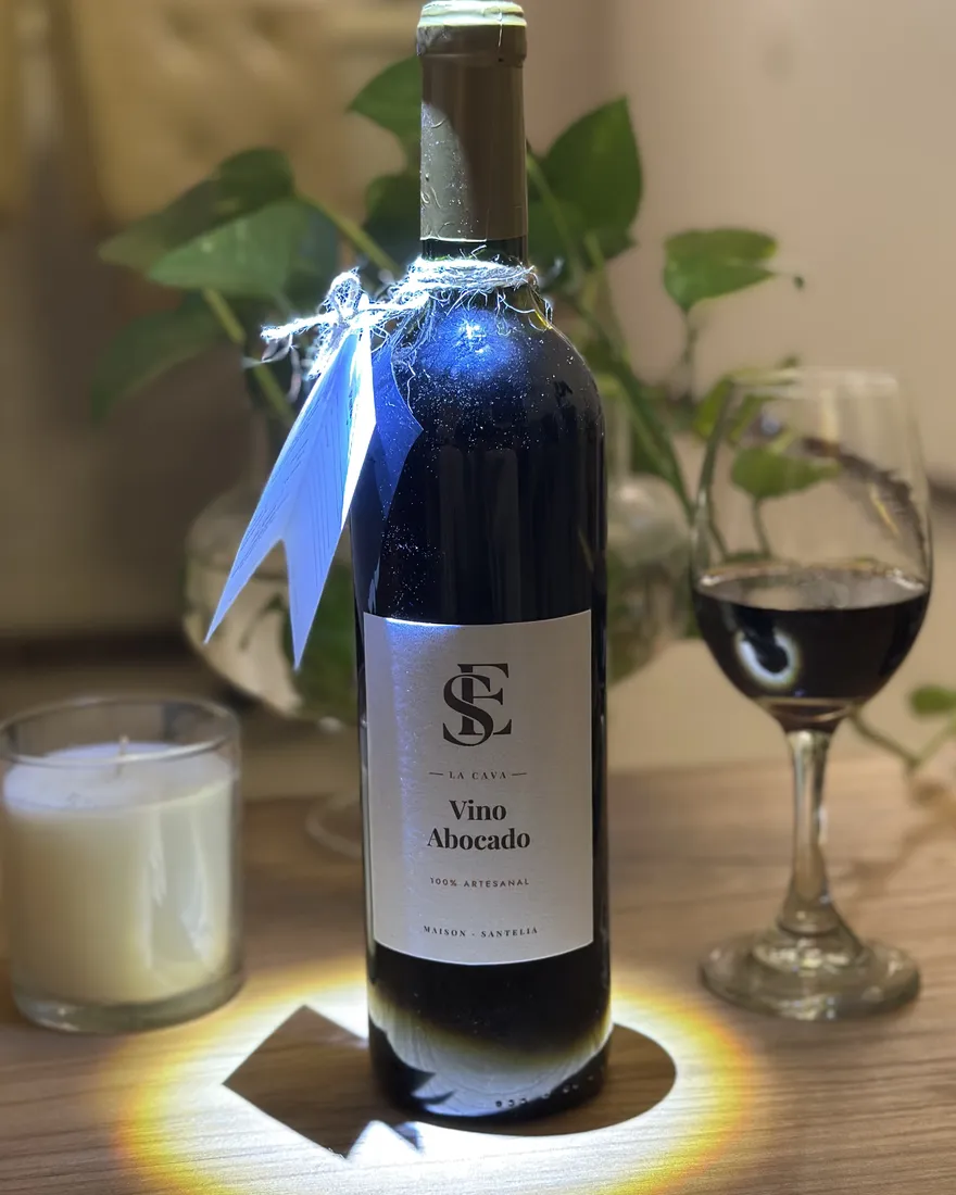 Botella de Vino abocado de La Cava con la etiqueta del monograma SE, junto a una copa de vino y una vela.