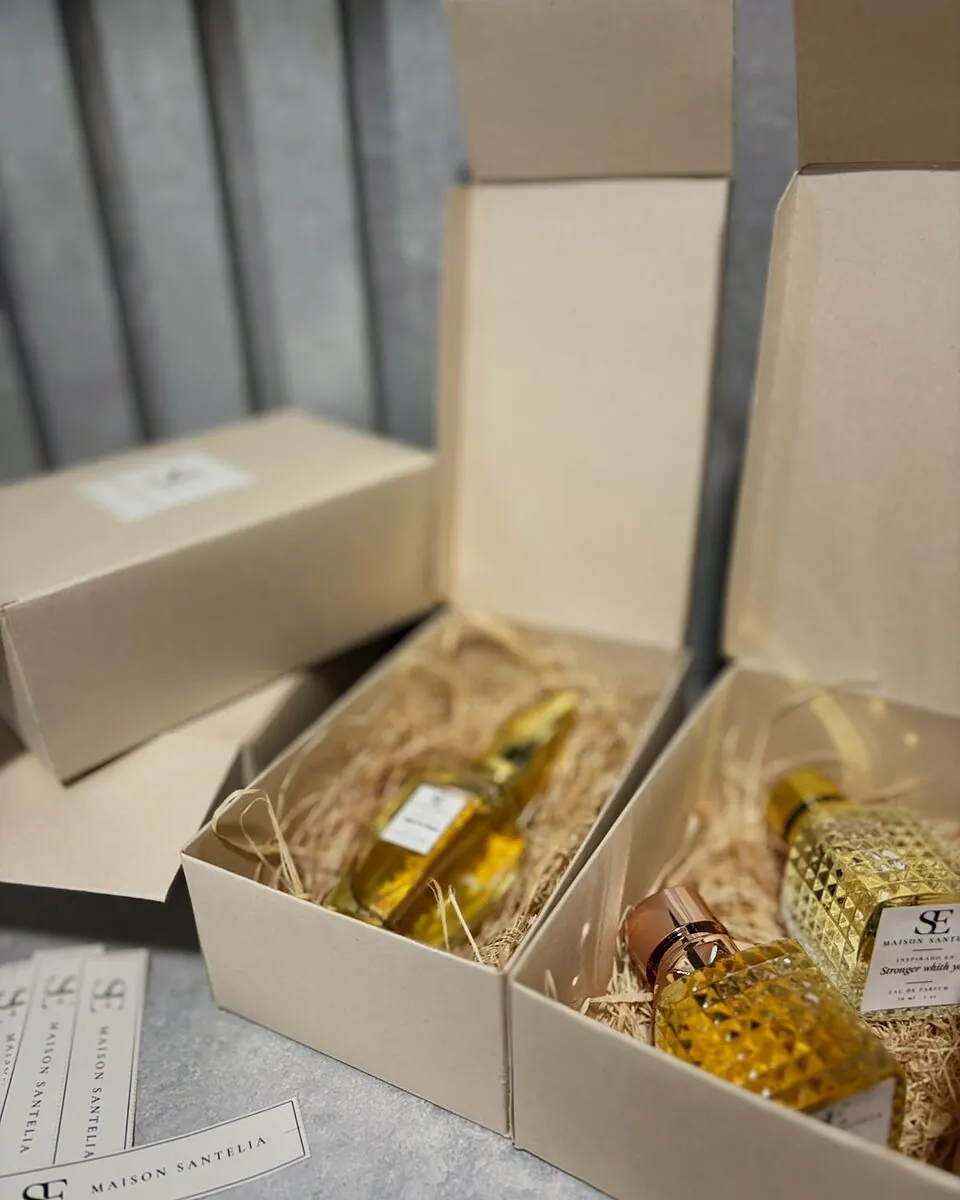 Cajas kraft abiertas con frascos de Maison Santelia sobre viruta, junto a etiquetas del monograma