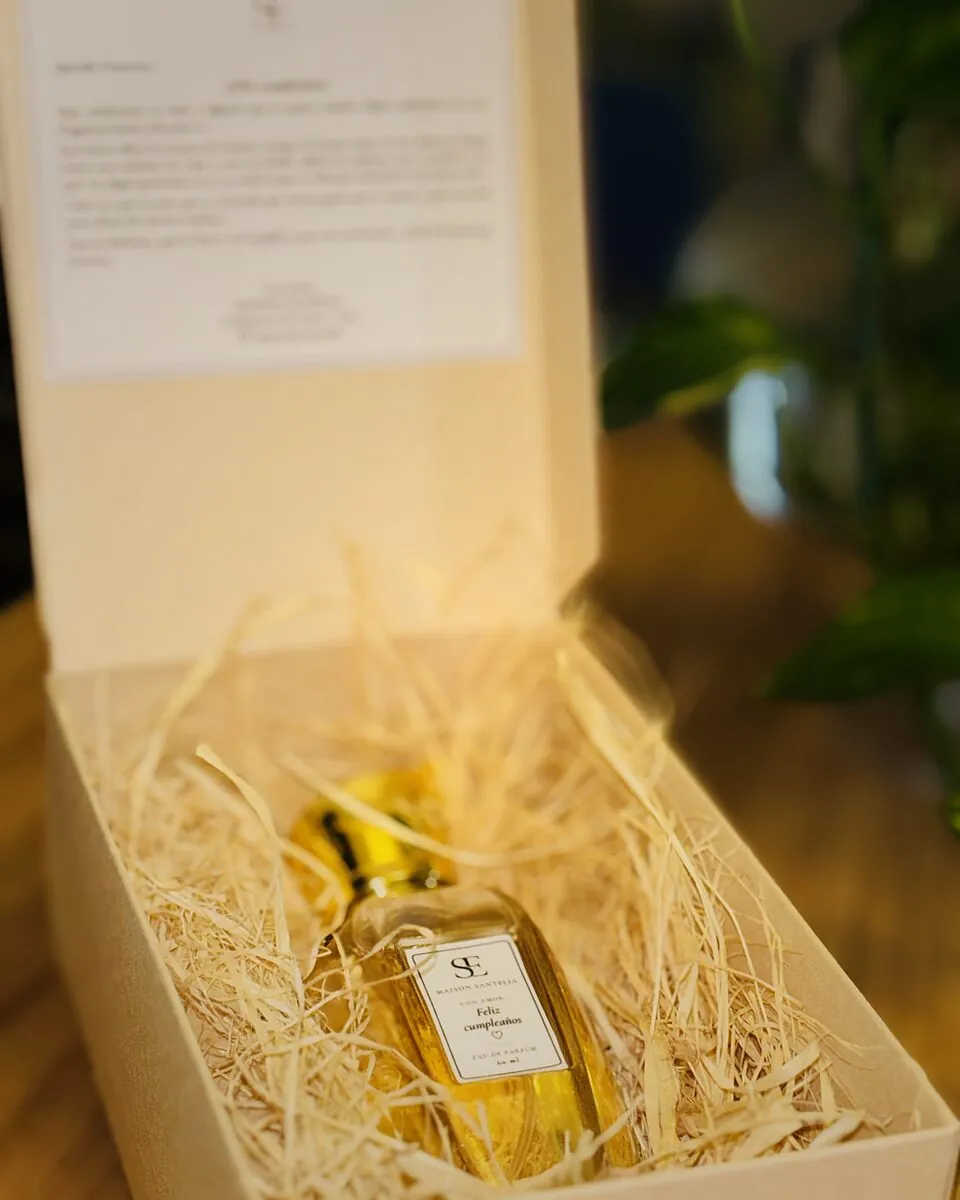Caja abierta con un frasco de 2 oz con etiqueta «Feliz cumpleaños», sobre viruta y con una carta